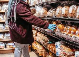 Side view of crop anonymous female customer picking loaf of bread in supermarket during coronavirus epidemic