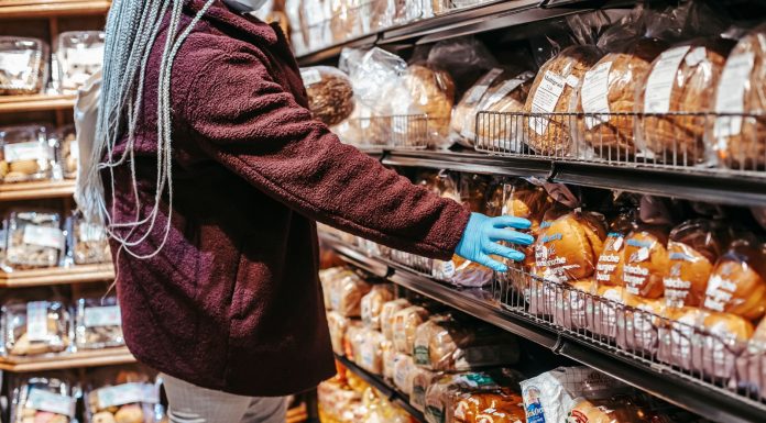 Side view of crop anonymous female customer picking loaf of bread in supermarket during coronavirus epidemic