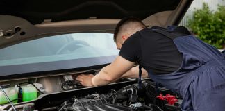 Auto mechanic performs engine maintenance on a car. Focus on hands and engine components.