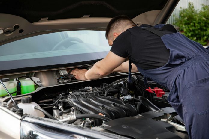 Auto mechanic performs engine maintenance on a car. Focus on hands and engine components.