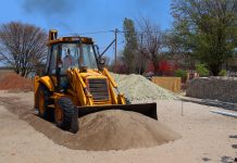 A yellow backhoe loader at a construction site moving sand on a clear day.
