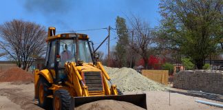 A yellow backhoe loader at a construction site moving sand on a clear day.