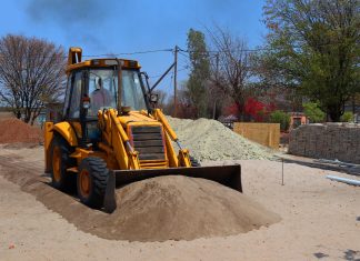 A yellow backhoe loader at a construction site moving sand on a clear day.