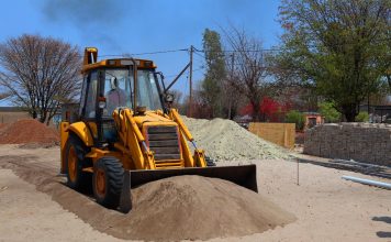 A yellow backhoe loader at a construction site moving sand on a clear day.