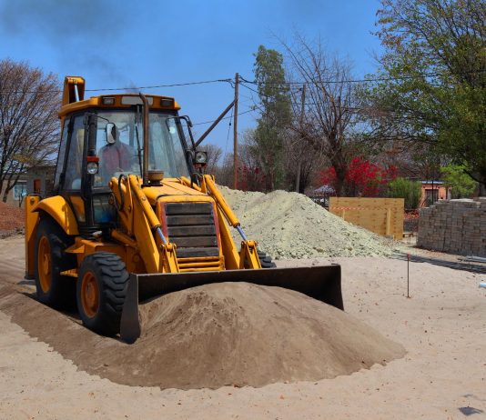 A yellow backhoe loader at a construction site moving sand on a clear day.