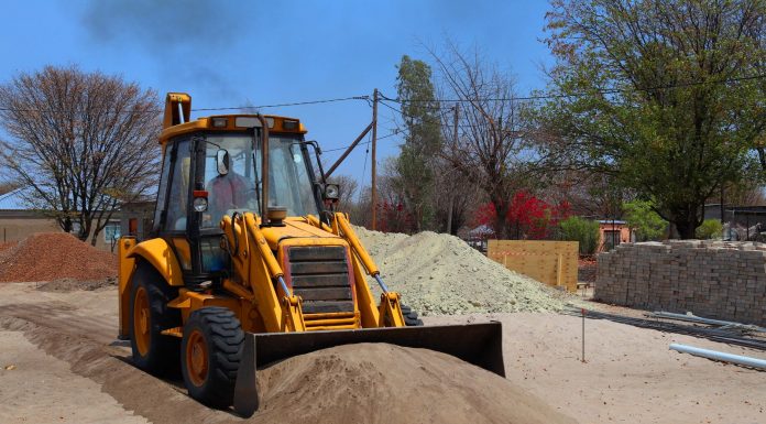 A yellow backhoe loader at a construction site moving sand on a clear day.