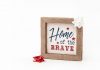 Patriotic framed sign with 'Home of the Brave' text and festive bows, perfect for home decor.