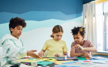 Children focusing on an art project with colored papers in a playful art class setting.