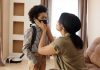A mother helps her young son wear a face mask, creating a touching family moment indoors.