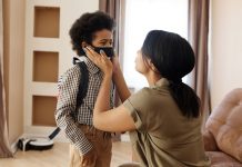A mother helps her young son wear a face mask, creating a touching family moment indoors.