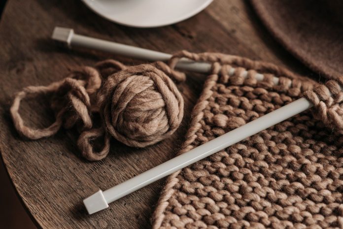 A close-up shot of cozy brown yarn and needles on a wooden table, showcasing knitting in progress.