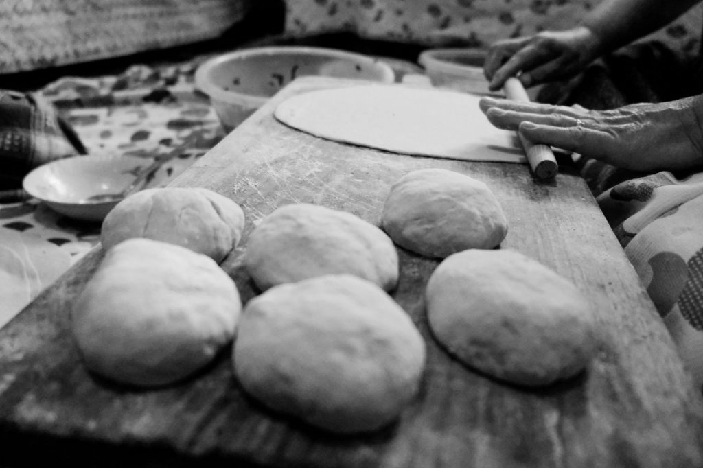 Black and white image of hands rolling dough in a traditional setting.