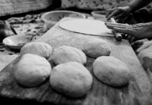 Black and white image of hands rolling dough in a traditional setting.
