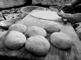 Black and white image of hands rolling dough in a traditional setting.