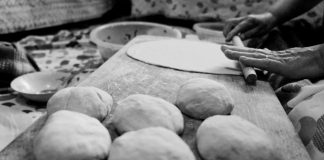 Black and white image of hands rolling dough in a traditional setting.