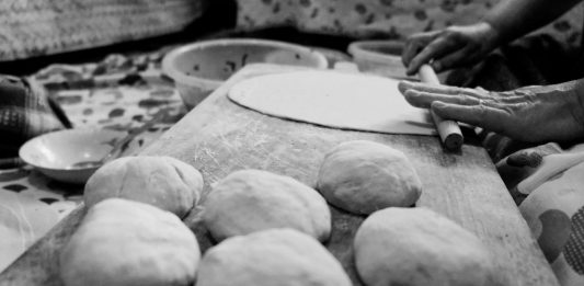Black and white image of hands rolling dough in a traditional setting.