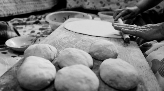 Black and white image of hands rolling dough in a traditional setting.