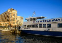 NY Waterway ferry docking at Hoboken, NJ against a clear blue sky, showcasing urban architecture.