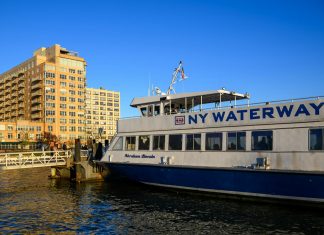 NY Waterway ferry docking at Hoboken, NJ against a clear blue sky, showcasing urban architecture.
