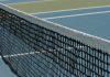Detailed perspective of a tennis net casting shadows on a vibrant blue court under sunlight.