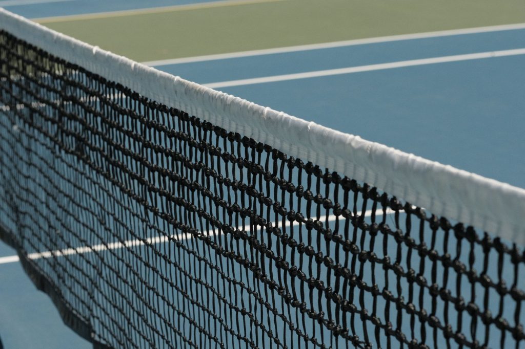 Detailed perspective of a tennis net casting shadows on a vibrant blue court under sunlight.