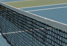 Detailed perspective of a tennis net casting shadows on a vibrant blue court under sunlight.
