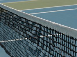 Detailed perspective of a tennis net casting shadows on a vibrant blue court under sunlight.