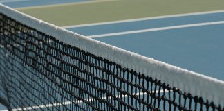 Detailed perspective of a tennis net casting shadows on a vibrant blue court under sunlight.