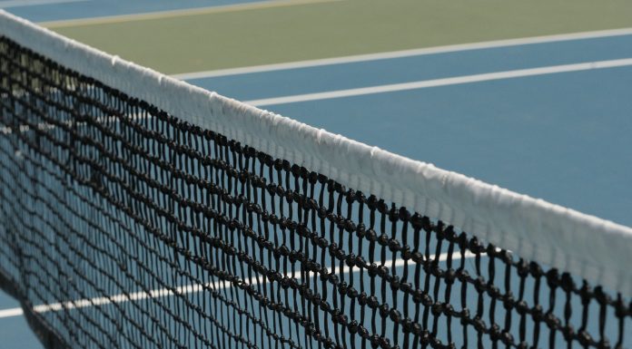 Detailed perspective of a tennis net casting shadows on a vibrant blue court under sunlight.