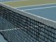 Detailed perspective of a tennis net casting shadows on a vibrant blue court under sunlight.