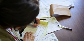 13,500 Jersey City Residents Face Loss of Medicaid or Food Benefits Under New Law A doctor fills out medical forms indoors, focusing on patient care and documentation.