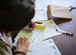 13,500 Jersey City Residents Face Loss of Medicaid or Food Benefits Under New Law A doctor fills out medical forms indoors, focusing on patient care and documentation.