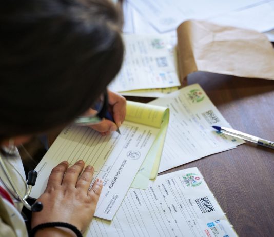 13,500 Jersey City Residents Face Loss of Medicaid or Food Benefits Under New Law A doctor fills out medical forms indoors, focusing on patient care and documentation.