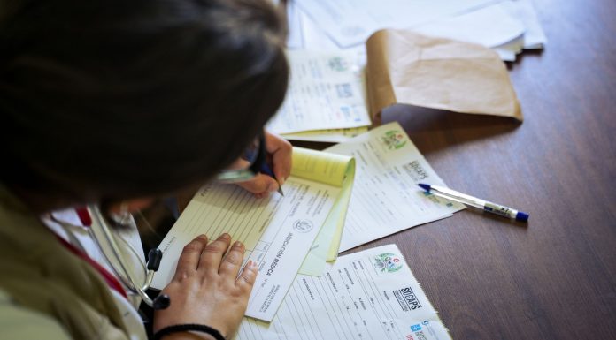 A doctor fills out medical forms indoors, focusing on patient care and documentation.