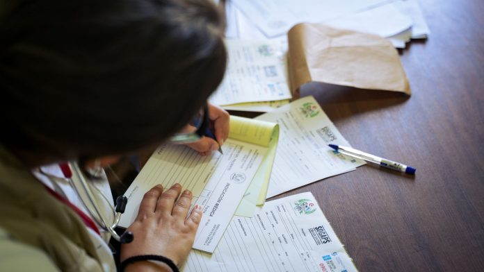 A doctor fills out medical forms indoors, focusing on patient care and documentation.