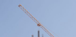 Tower crane working on a high-rise building construction site against a clear blue sky.
