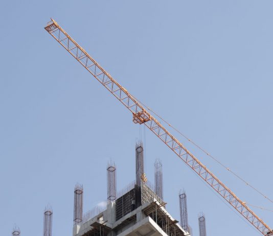 Tower crane working on a high-rise building construction site against a clear blue sky.