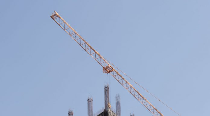 27-Story Tower Approved for Hoboken’s Five Corners, Hindu Temple to Move Tower crane working on a high-rise building construction site against a clear blue sky.