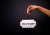 50 New Businesses Headed to Jersey City and Hoboken by Summer 2026 Close-up of a hand holding a 'We are open' sign against a black background.