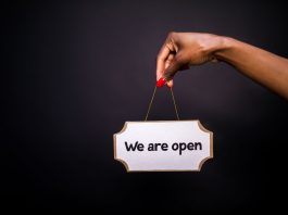 50 New Businesses Headed to Jersey City and Hoboken by Summer 2026 Close-up of a hand holding a 'We are open' sign against a black background.