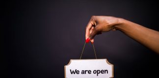 50 New Businesses Headed to Jersey City and Hoboken by Summer 2026 Close-up of a hand holding a 'We are open' sign against a black background.