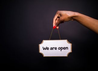 Close-up of a hand holding a 'We are open' sign against a black background.