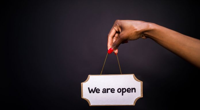 Close-up of a hand holding a 'We are open' sign against a black background.
