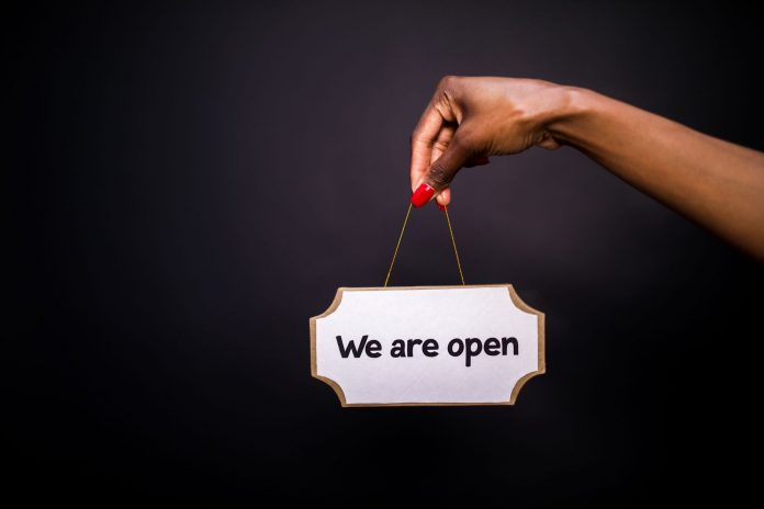 50-new-businesses-headed-to-jersey-city-and-hoboke Close-up of a hand holding a 'We are open' sign against a black background.