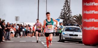 Two male athletes racing in a marathon with a cheering crowd and bright finish line.