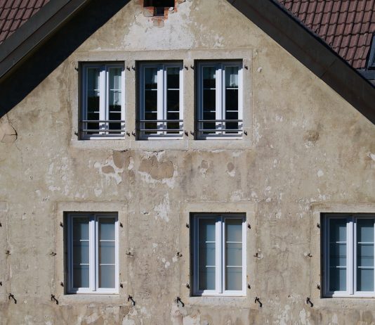 A Century in Jersey City, Now Fearing the End Close-up of an aged European house facade with multiple windows and rustic texture.