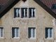 A Century in Jersey City, Now Fearing the End Close-up of an aged European house facade with multiple windows and rustic texture.