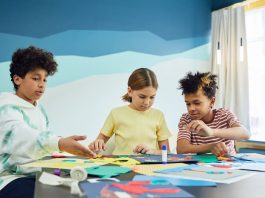 Children focusing on an art project with colored papers in a playful art class setting.
