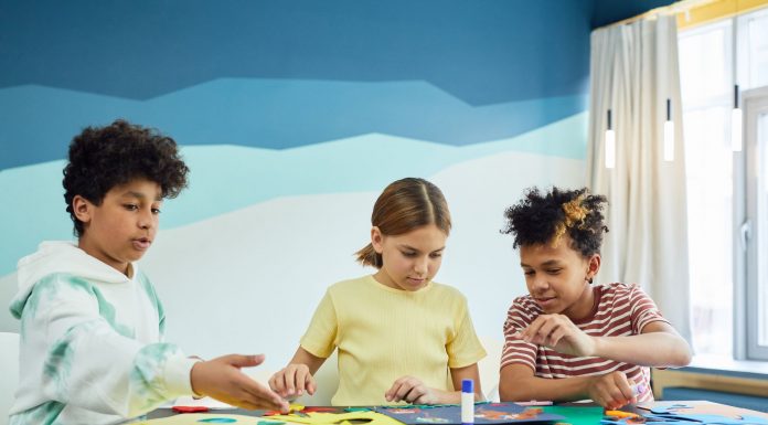 Children focusing on an art project with colored papers in a playful art class setting.
