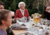Smiling elderly woman with family and friends enjoying dinner at table backyard garden